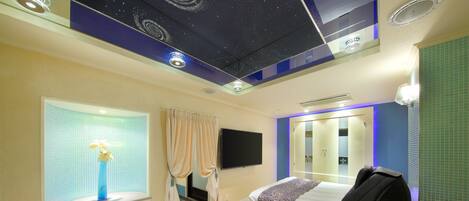 Una habitación de hotel con cama, sillón de masajes, televisor y ventana con cortinas.