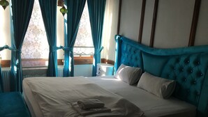 A bedroom with a large bed, blue curtains, and a view of the outdoors. - Kuscu Han Otel (Safranbolu)