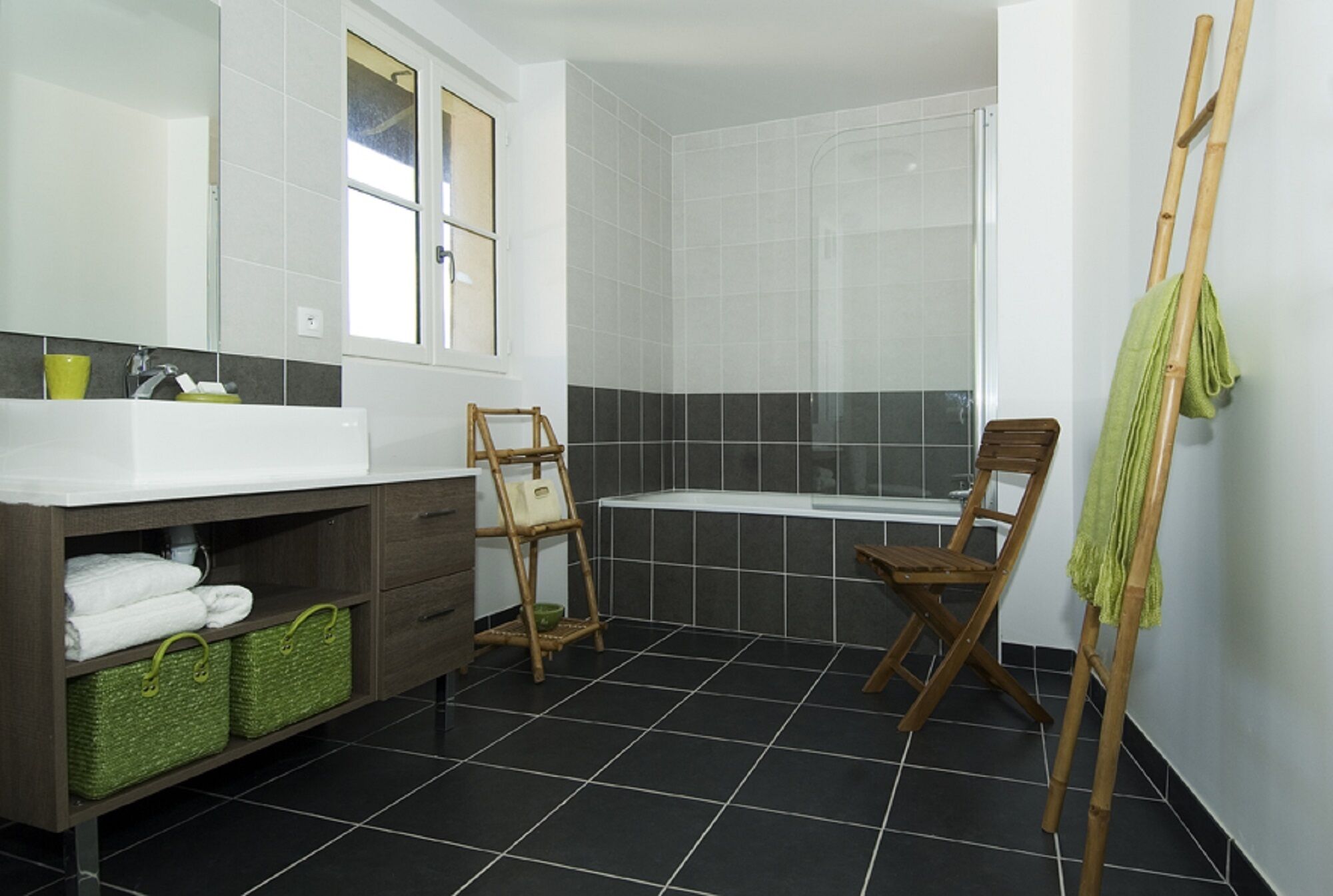 A bathroom with a bathtub, a wooden chair, a green towel, and a shelf with baskets.