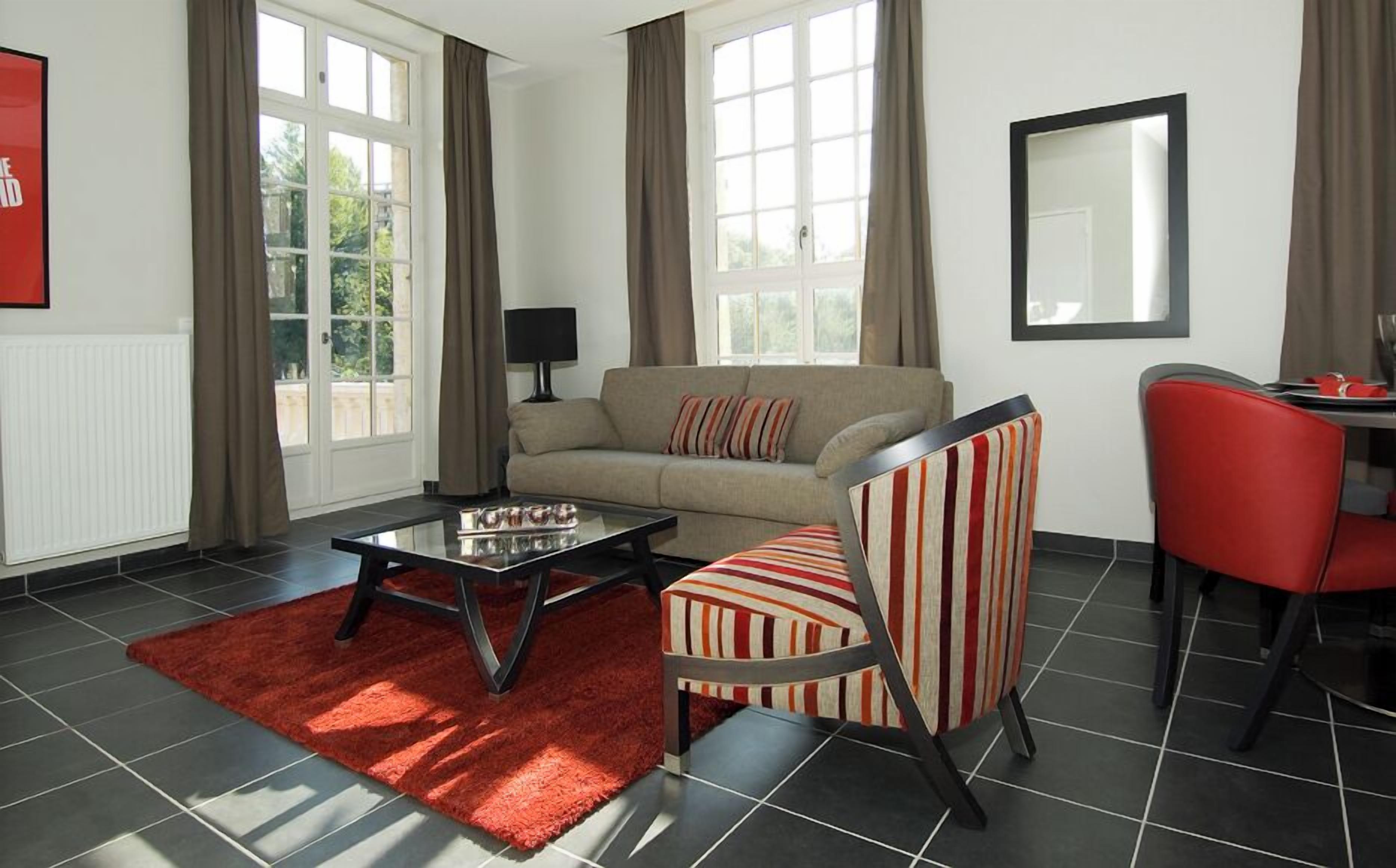 A modern living room with a sofa, a striped armchair, a glass coffee table, and a red rug.