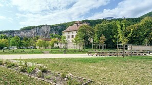 Um parque com mesas para piquenique, um edifício com telhado vermelho e uma montanha ao fundo.
