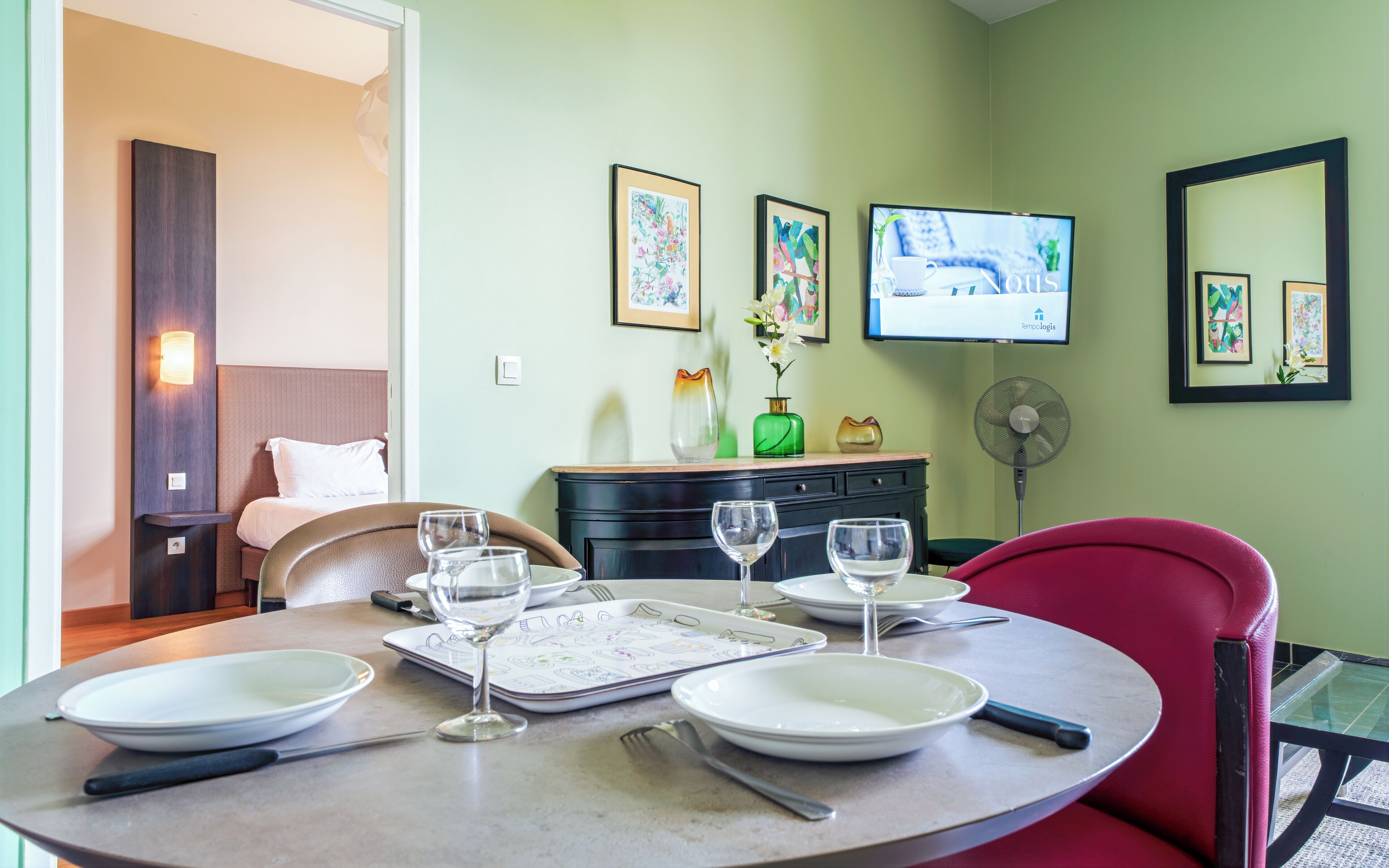 A dining area with a round table, chairs, and a television mounted on the wall.
