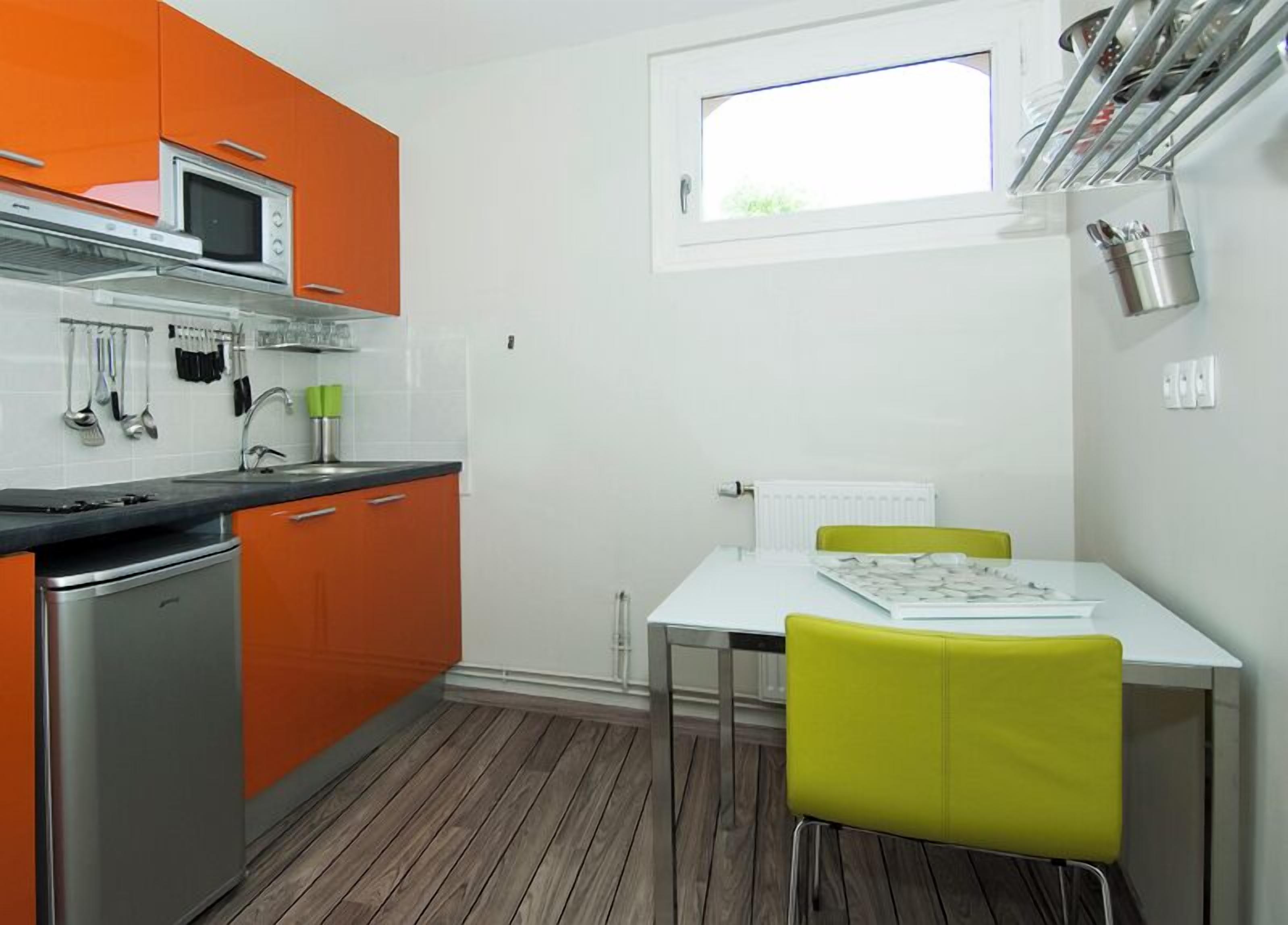 A compact kitchen with orange cabinets, a microwave, and a stove. There's a small dining table with a chair and a window above it.