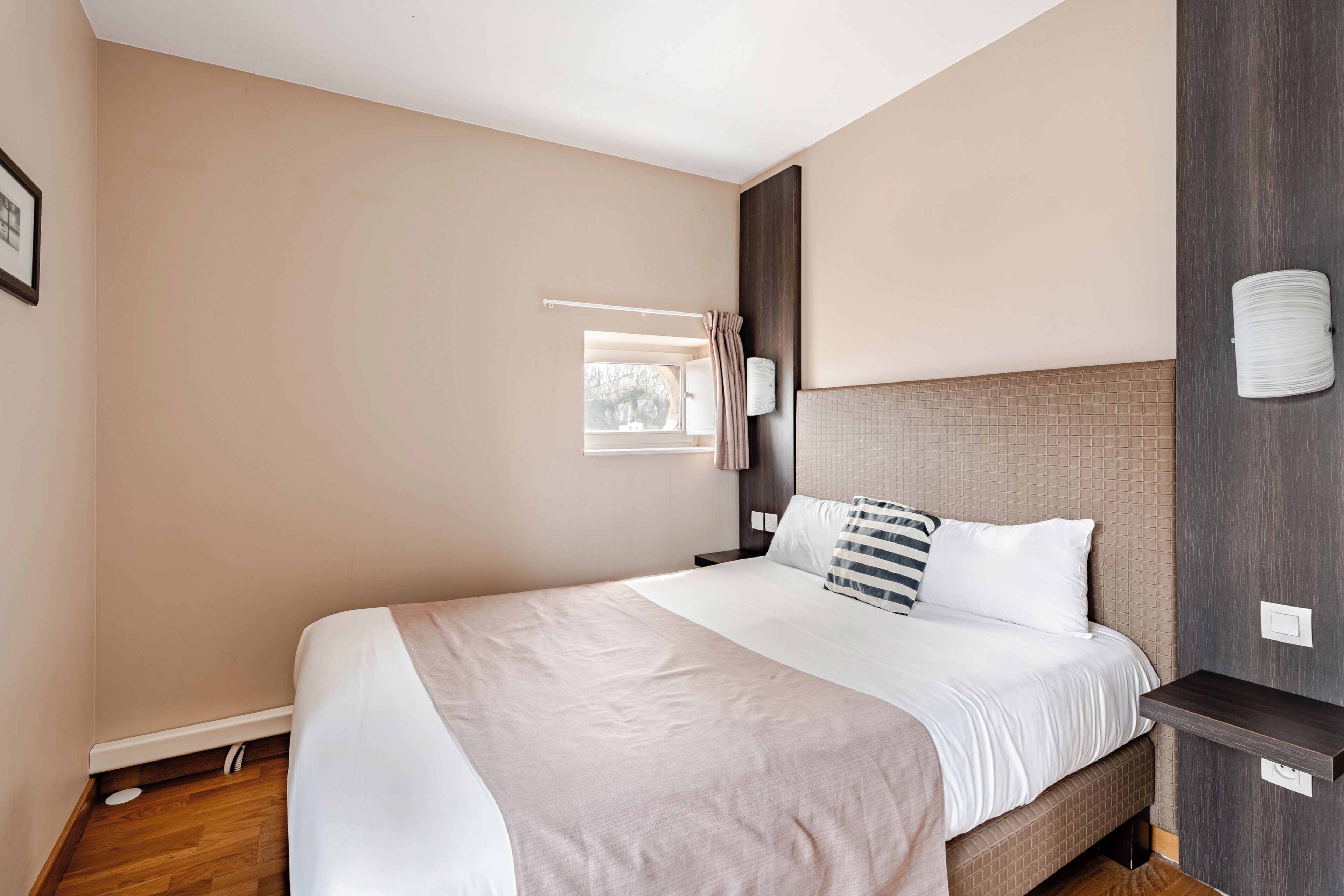 Een moderne hotelkamer met een groot bed, een nachtkastje, een wandlamp en een raam met gordijnen.
