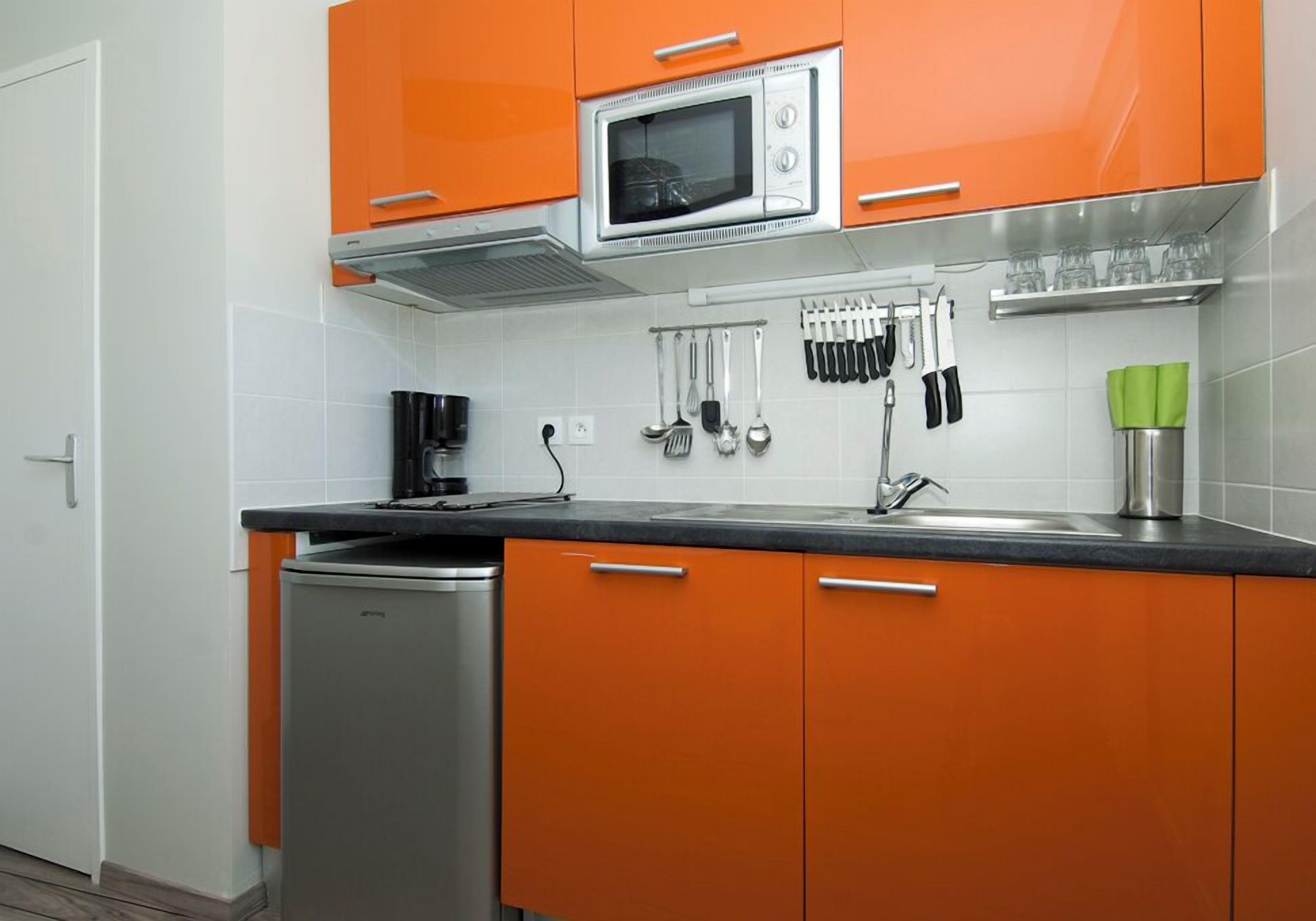 A kitchen with orange cabinets, a microwave, and various utensils hanging on the wall.