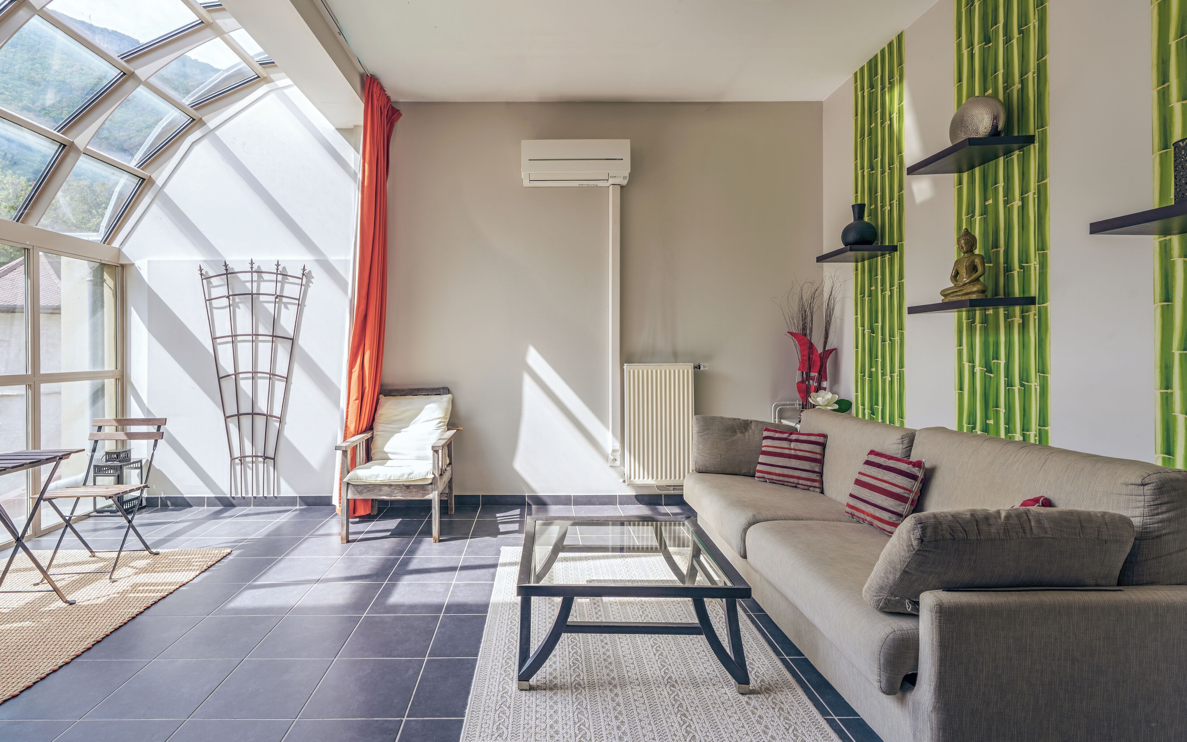 Una sala de estar con sofá, mesa de centro, silla, radiador y ventana con cortinas.