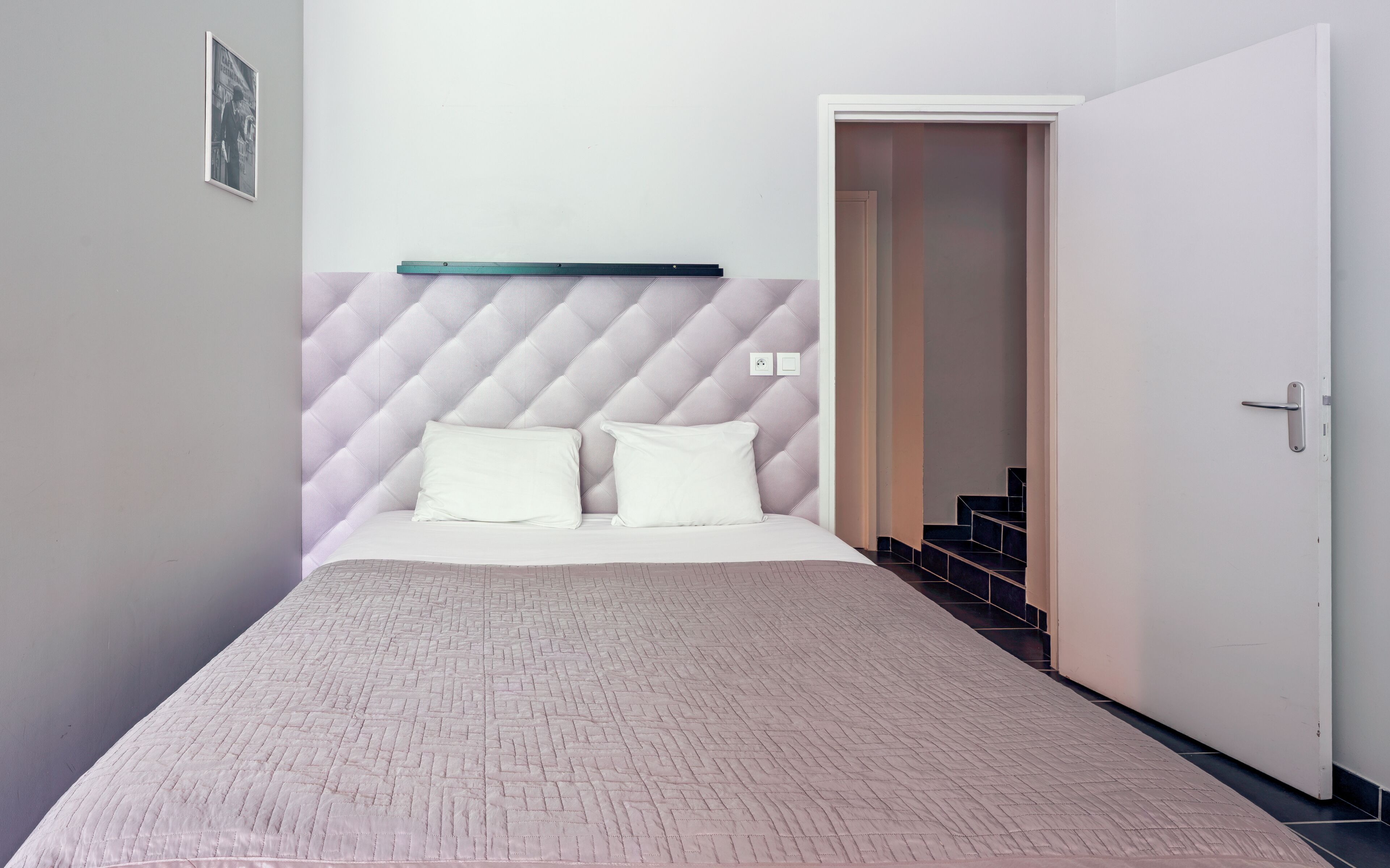 Un dormitorio con cama, cabecera, una puerta y una escalera.
