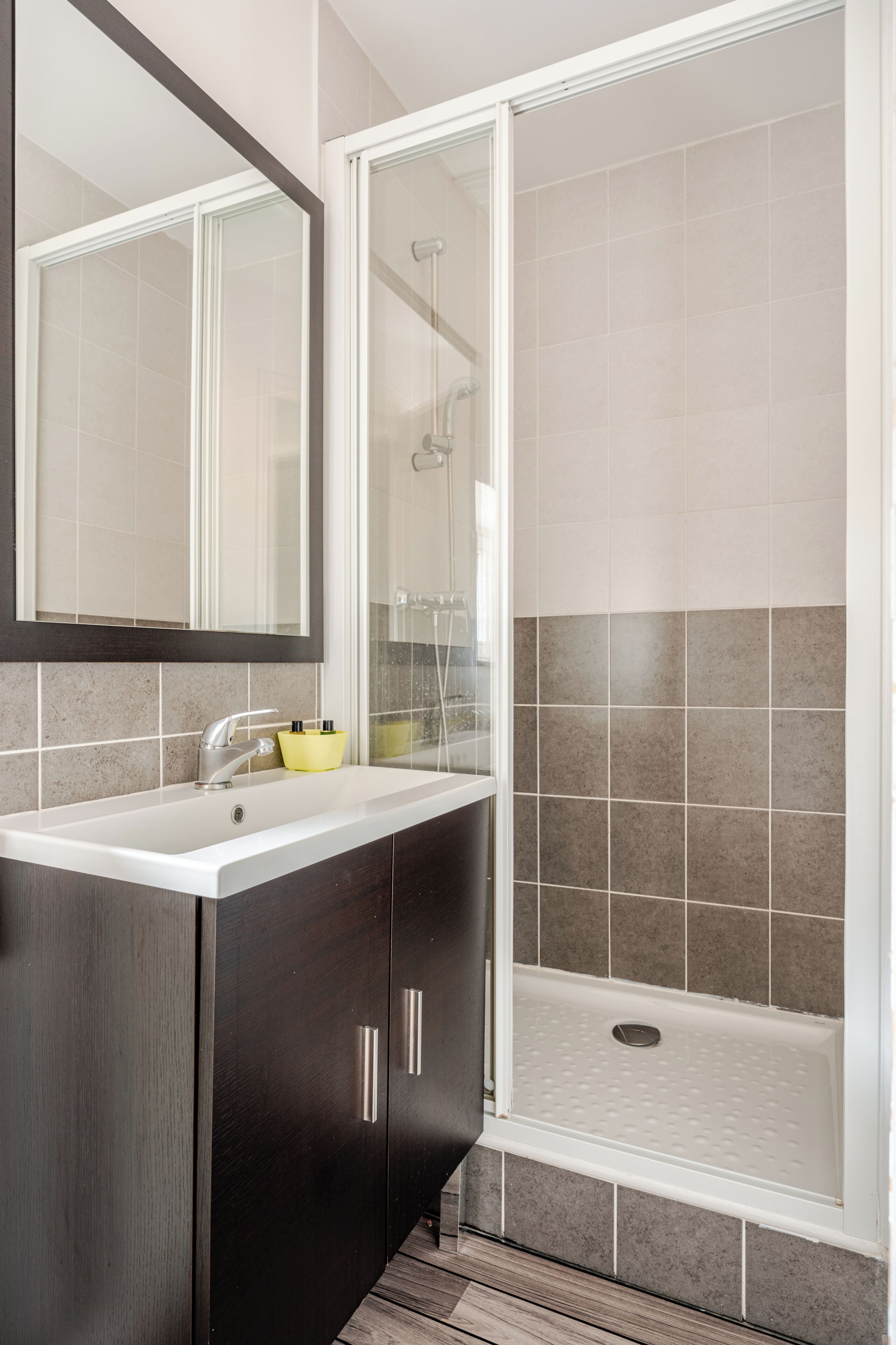 Un baño con lavamanos blanco, muebles oscuros, un espejo y una zona de ducha.