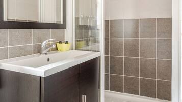 Un baño con lavamanos blanco, muebles oscuros, un espejo y una zona de ducha.
