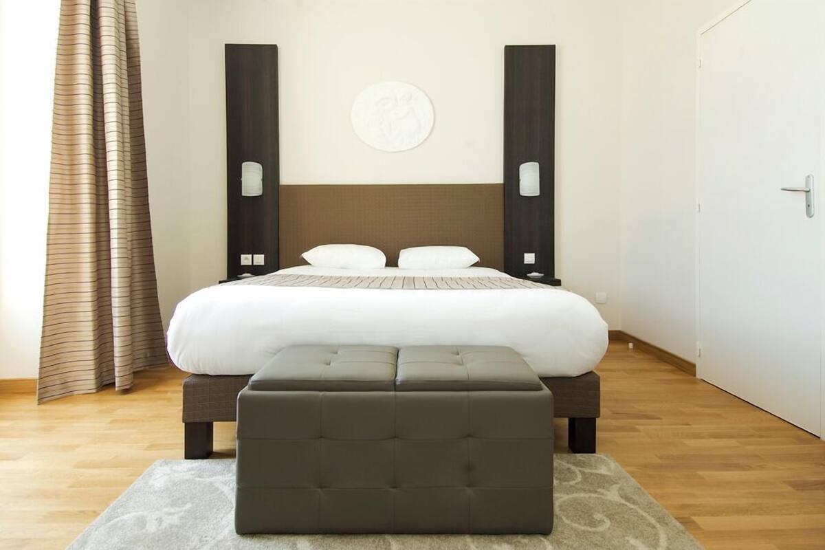 Quarto de hotel moderno com uma cama grande, um banco e uma obra de arte na parede.
