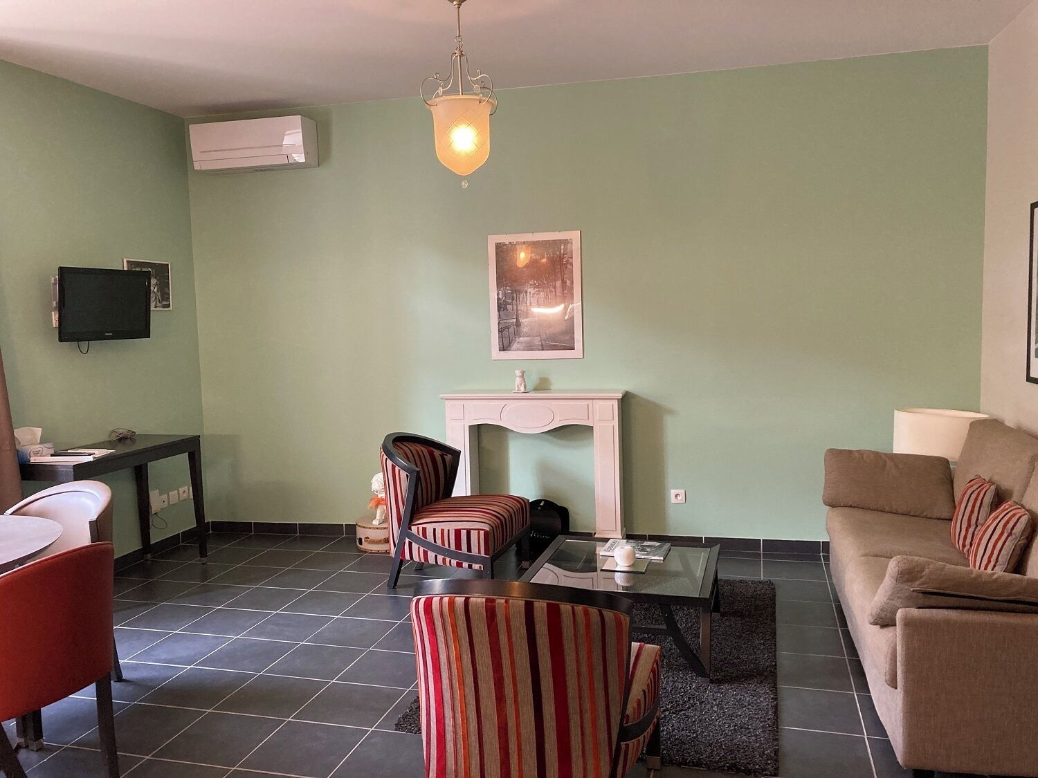 A living room with a fireplace, striped chairs, a sofa, a television, and a tiled floor.