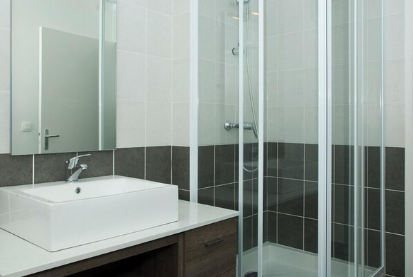 Un baño moderno con un lavamanos blanco, baldosas oscuras y un box de ducha de vidrio.