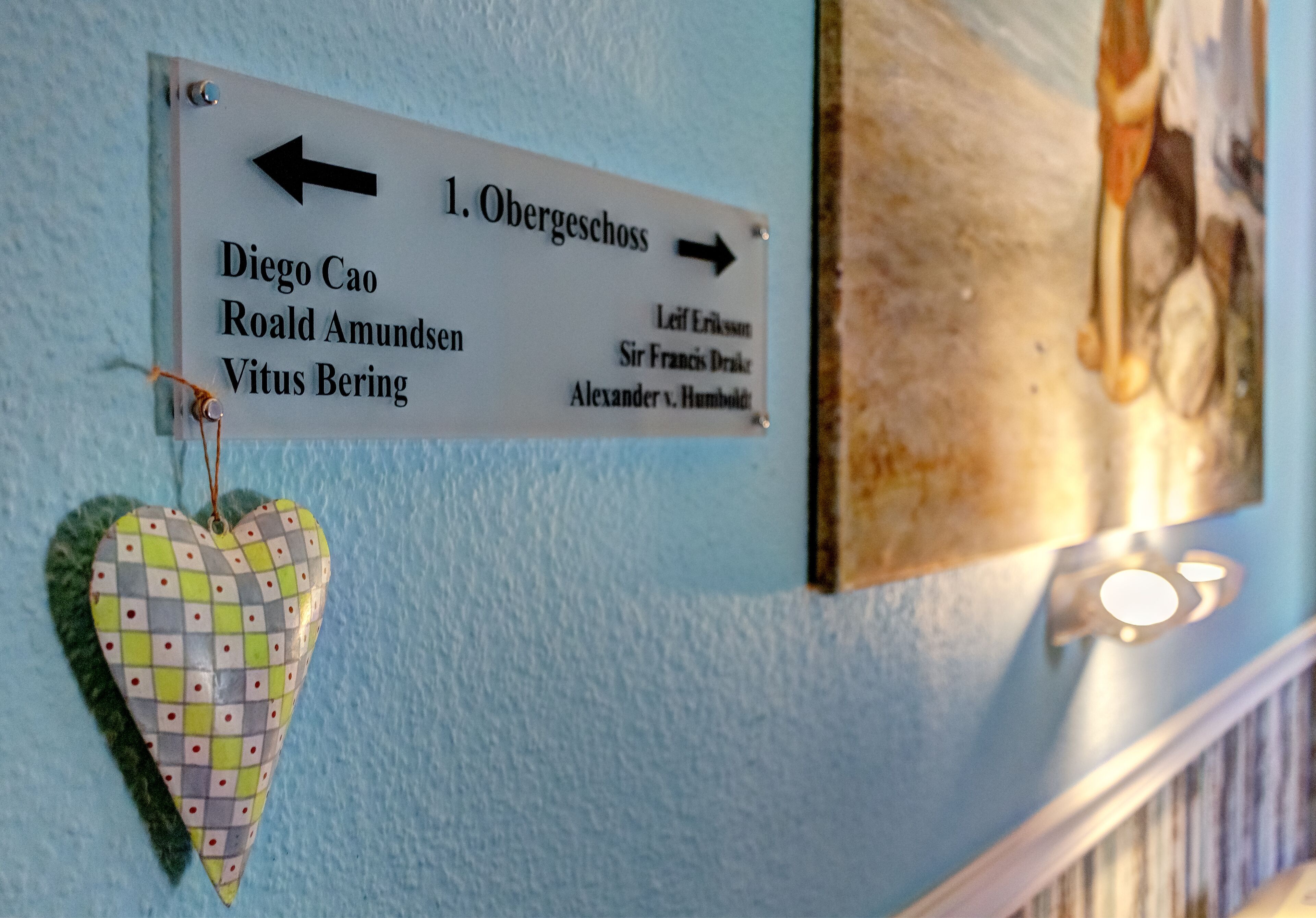 A directional sign with names and arrows, a heart-shaped decoration, and a wall-mounted light fixture.
