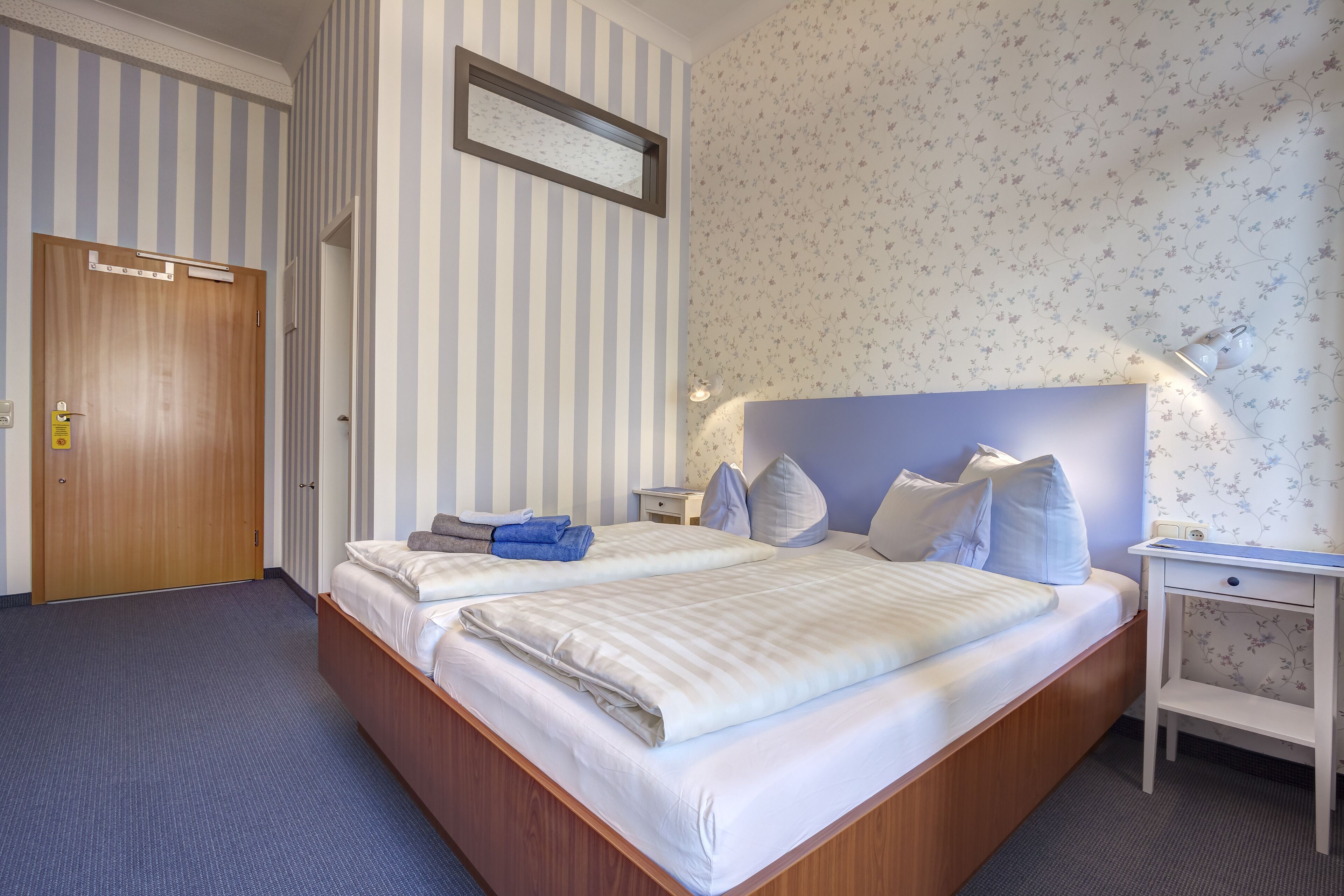 A hotel room with two beds, a wooden door, a nightstand, and a small desk.