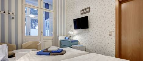 Habitación de hotel con dos camas, un escritorio, una silla, un televisor y una ventana con persianas.