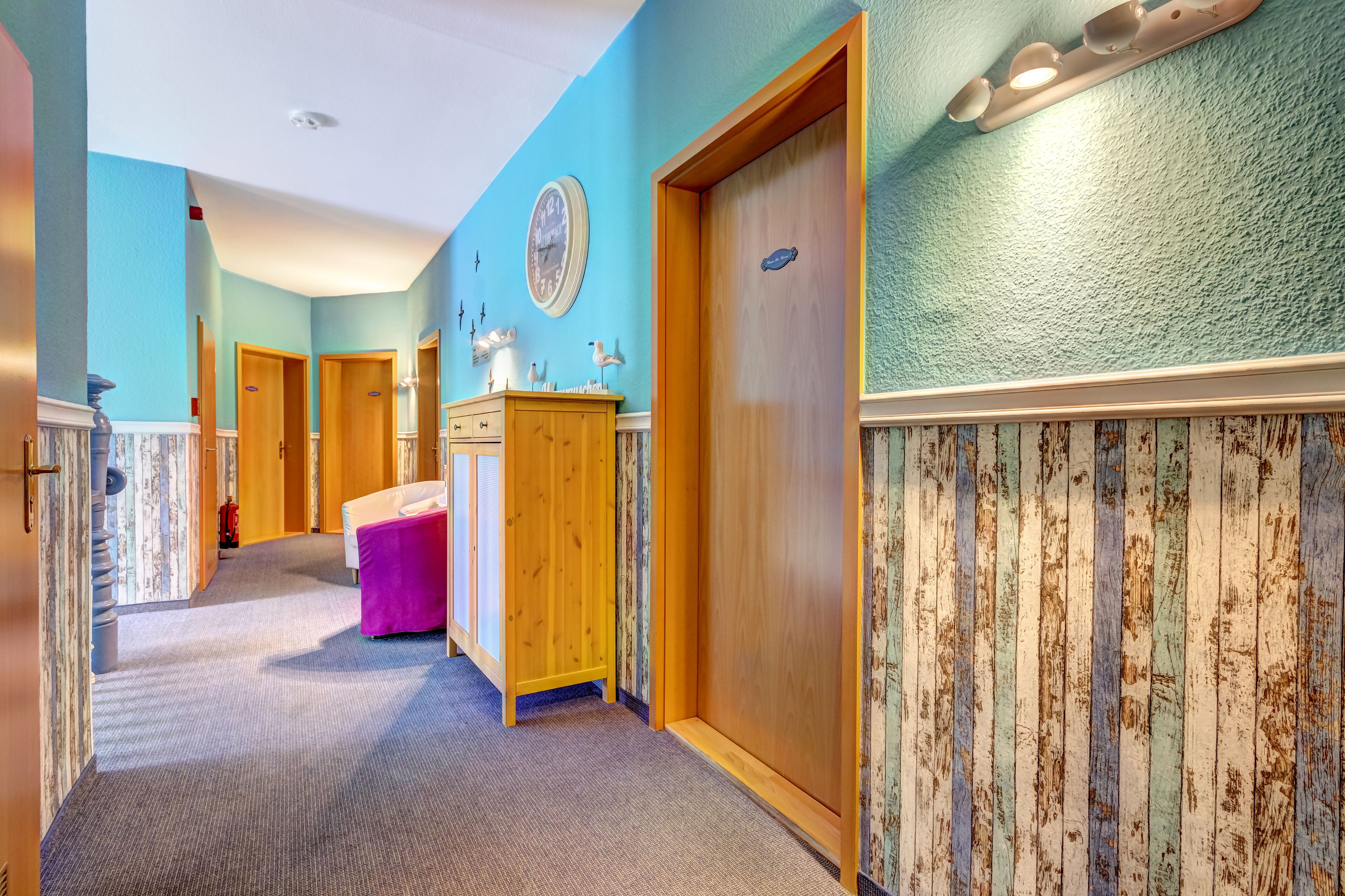 A hotel hallway with wooden doors, a wooden dresser, and a clock on the wall.