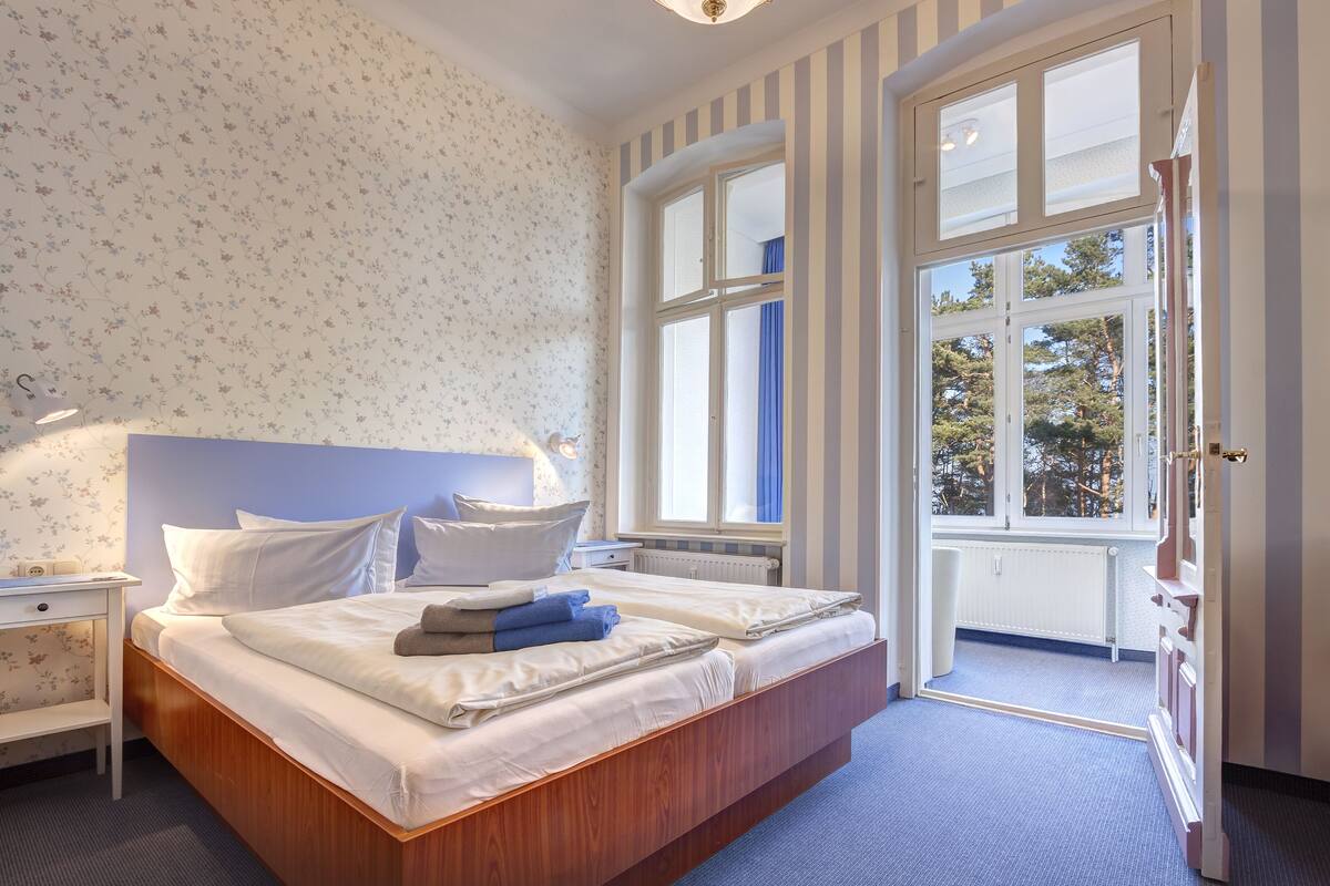 Un dormitorio con una cama grande, una mesita de noche, un aparador y una ventana con vistas a árboles.