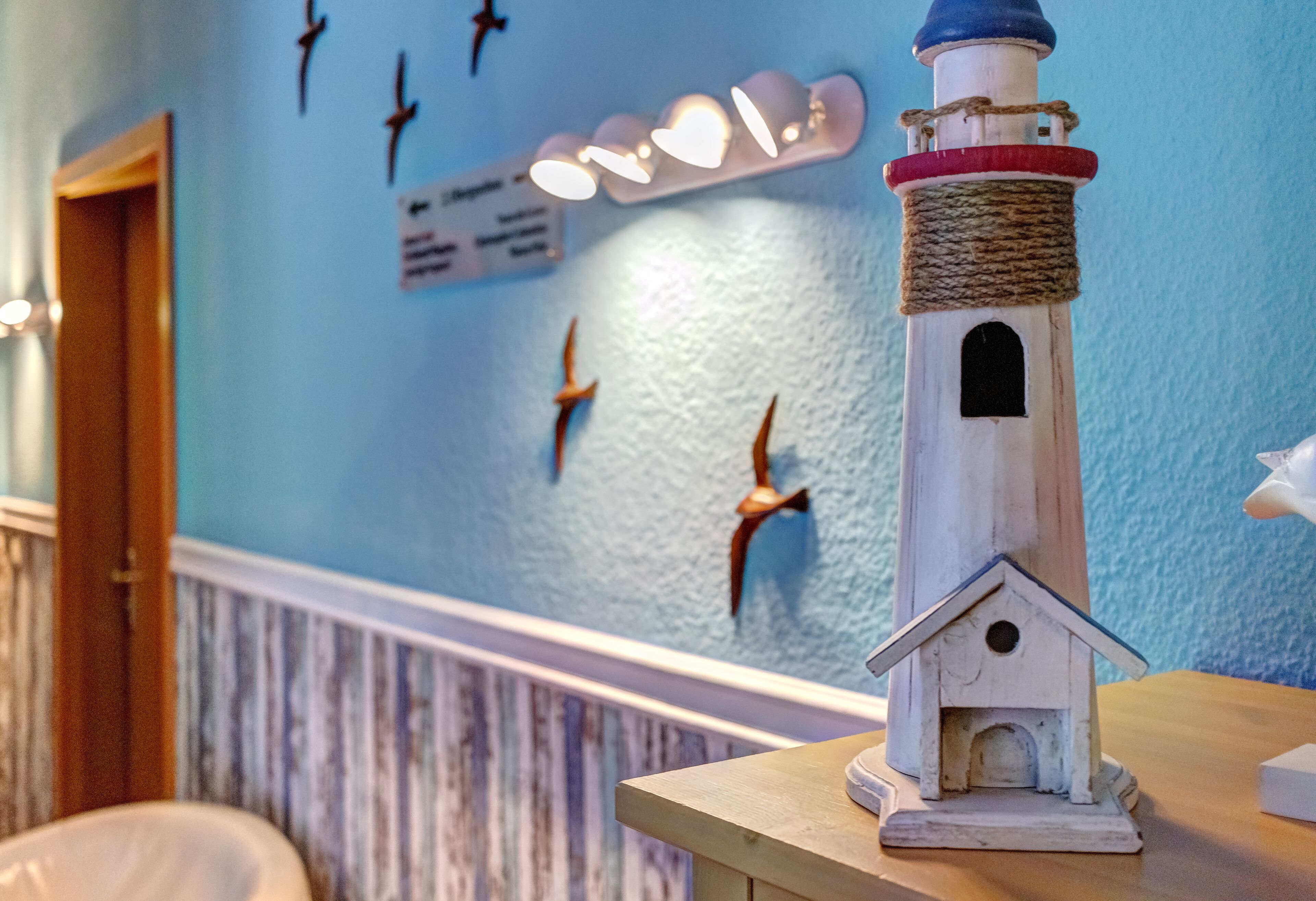A lighthouse model on a table, a wooden door, and a wall with bird decorations and a sign.