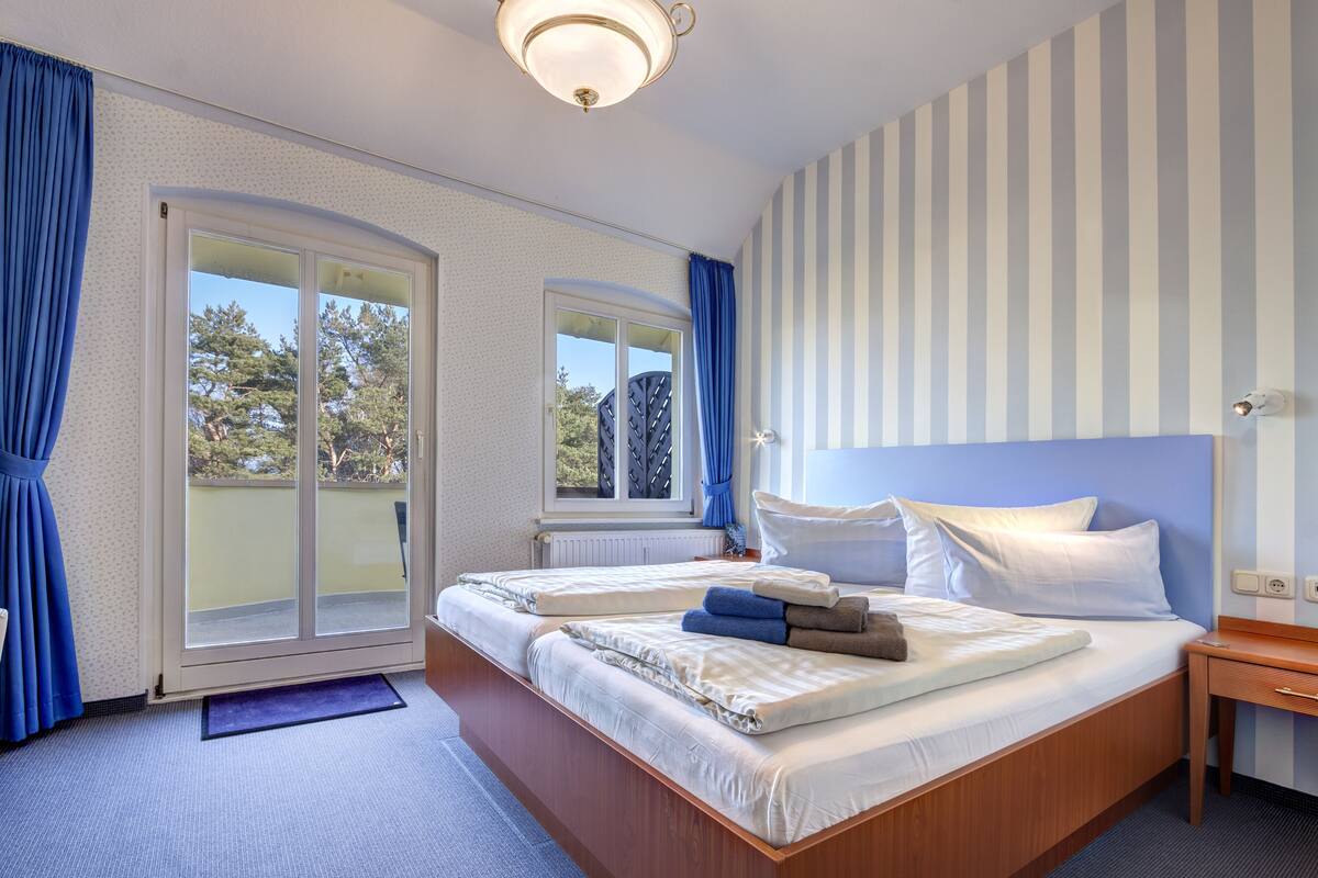 Un dormitorio con una cama grande, dos ventanas, un cabecero de madera y vistas a árboles.