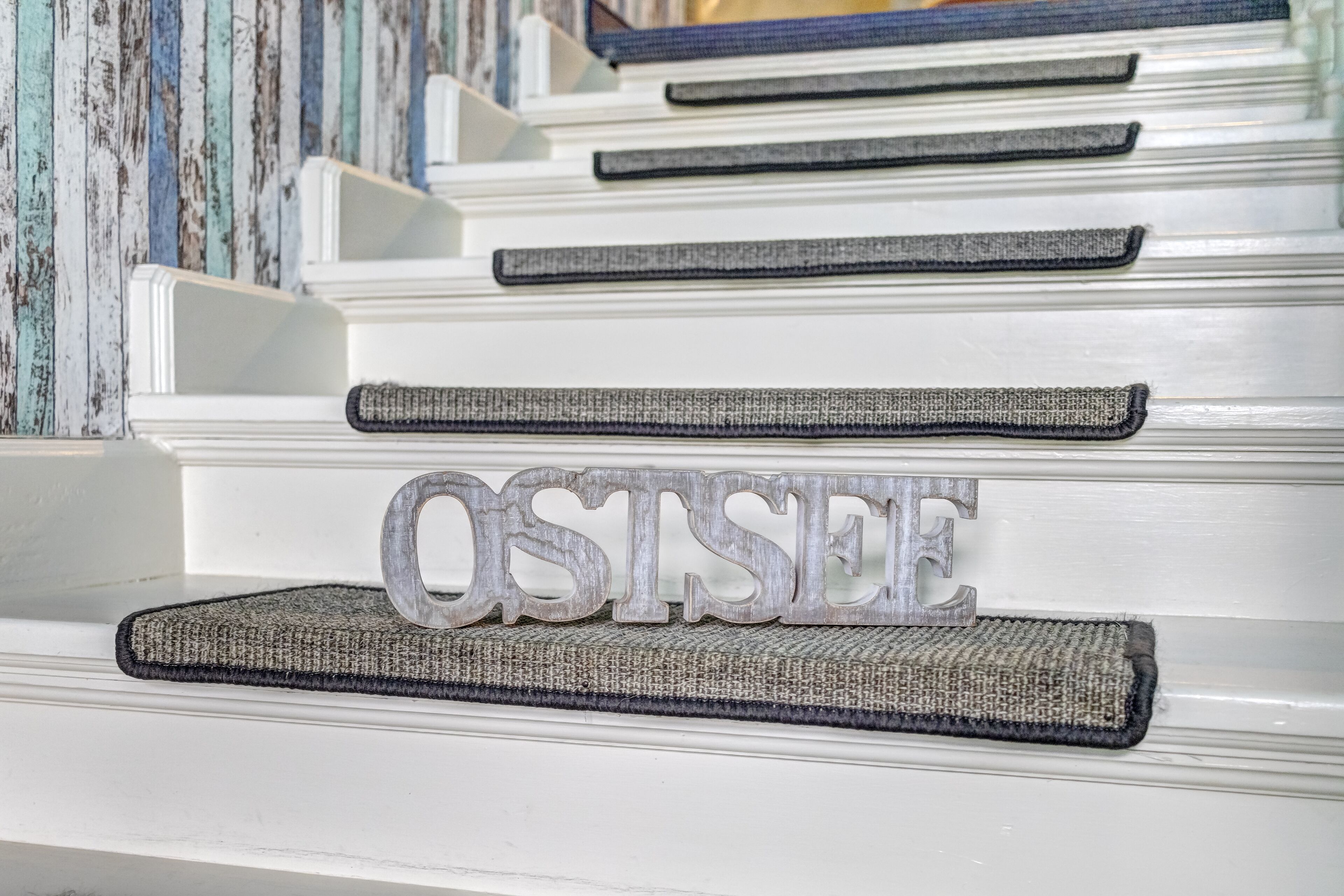 A staircase with a textured rug and a decorative sign spelling "OSTSEE" on the steps.