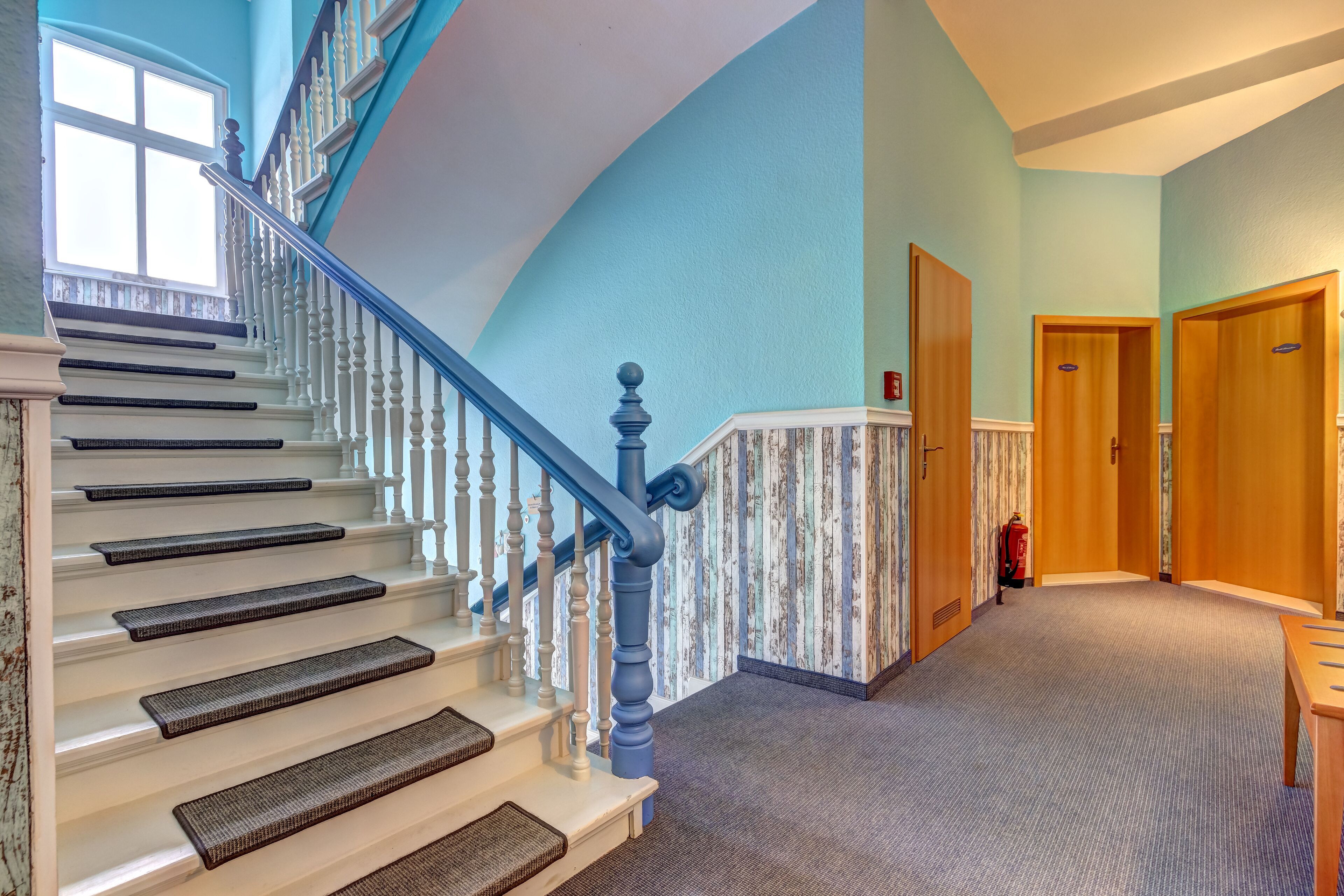 A hotel lobby with a staircase, wooden doors, and a fire extinguisher.