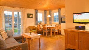 A cozy living room with a sofa, dining table, and chairs. There is a television on the wall and a cabinet with a radio. - Alpenrösle (Balderschwang)