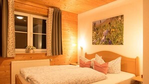 A bedroom with a wooden ceiling, a bed with floral bedding, a window with curtains, and a painting on the wall. - Alpenrösle (Balderschwang)