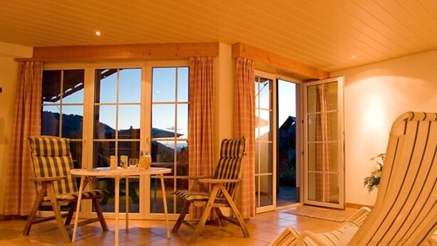 A cozy room with a wooden ceiling, a round table with chairs, and a sliding glass door leading outside. - Alpenrösle (Balderschwang)