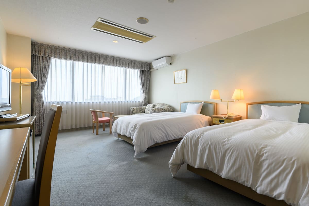 Ett hotellrum med två sängar, ett skrivbord med en dator, en stol och ett fönster med gardiner.