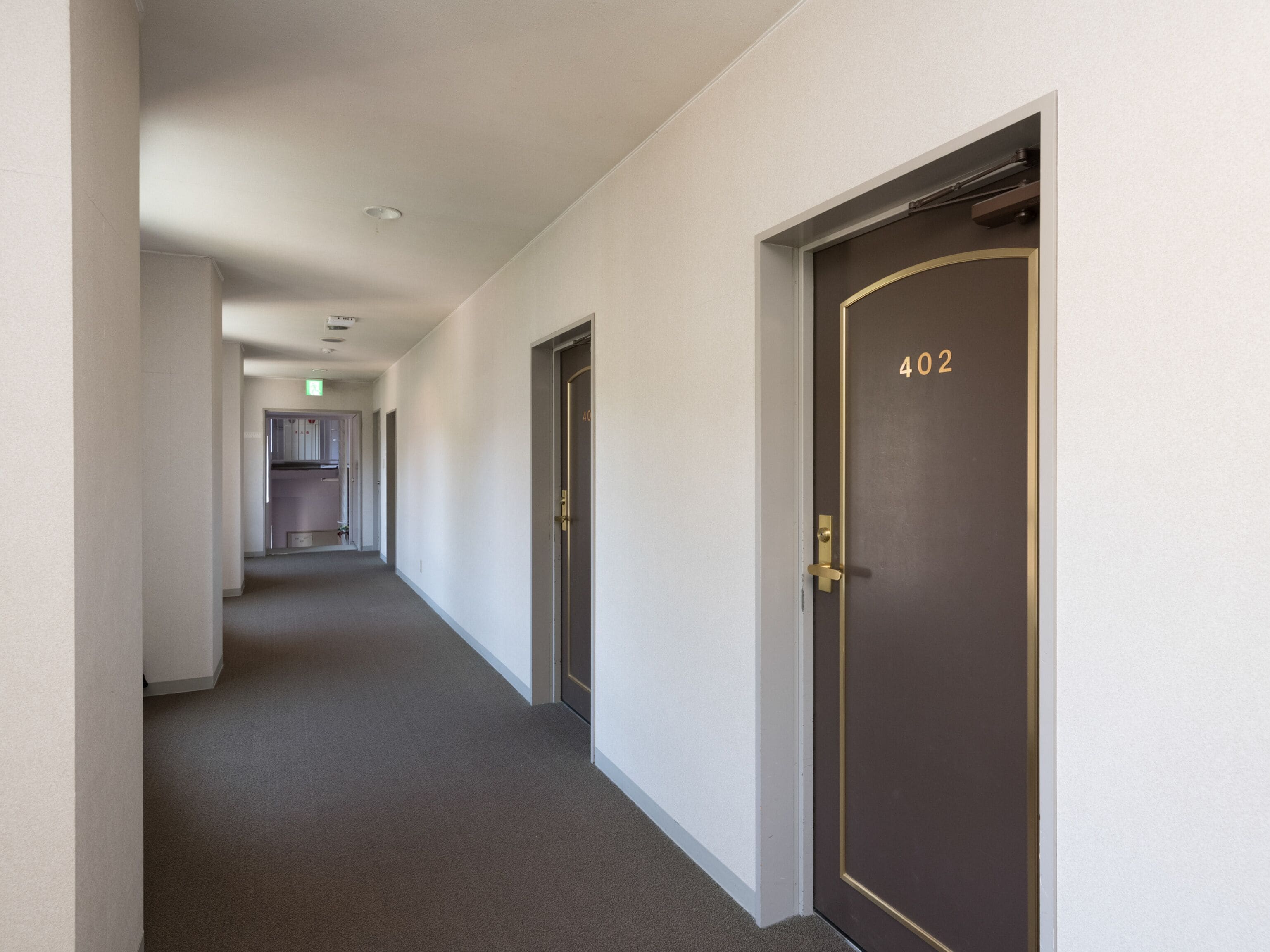 A hallway with a dark door marked "402" and a kitchen area in the distance.