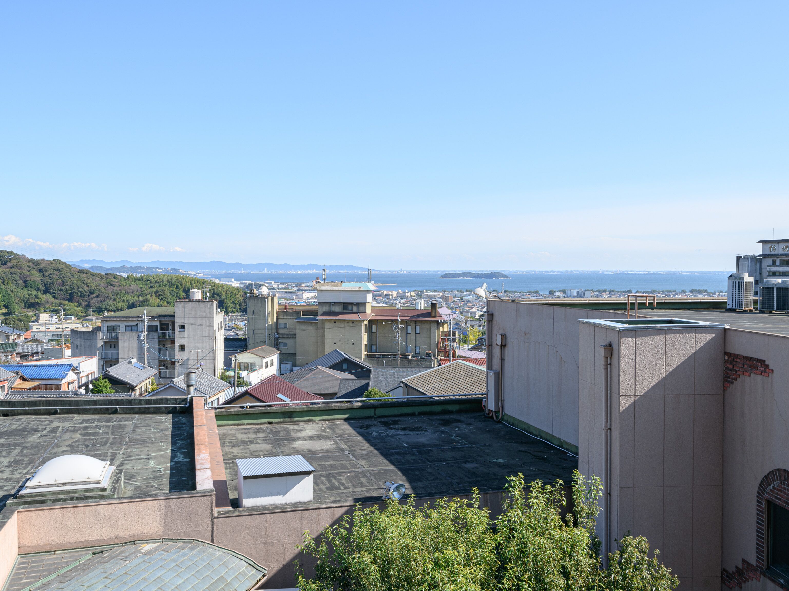 A rooftop with a view of a cityscape, including buildings and a distant island.