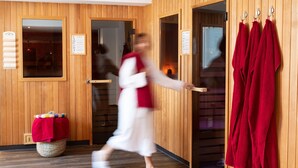 A wooden interior with a person in white attire opening a door to a sauna area, where red towels are hung on hooks. - Parkhotel Herne (Herne)