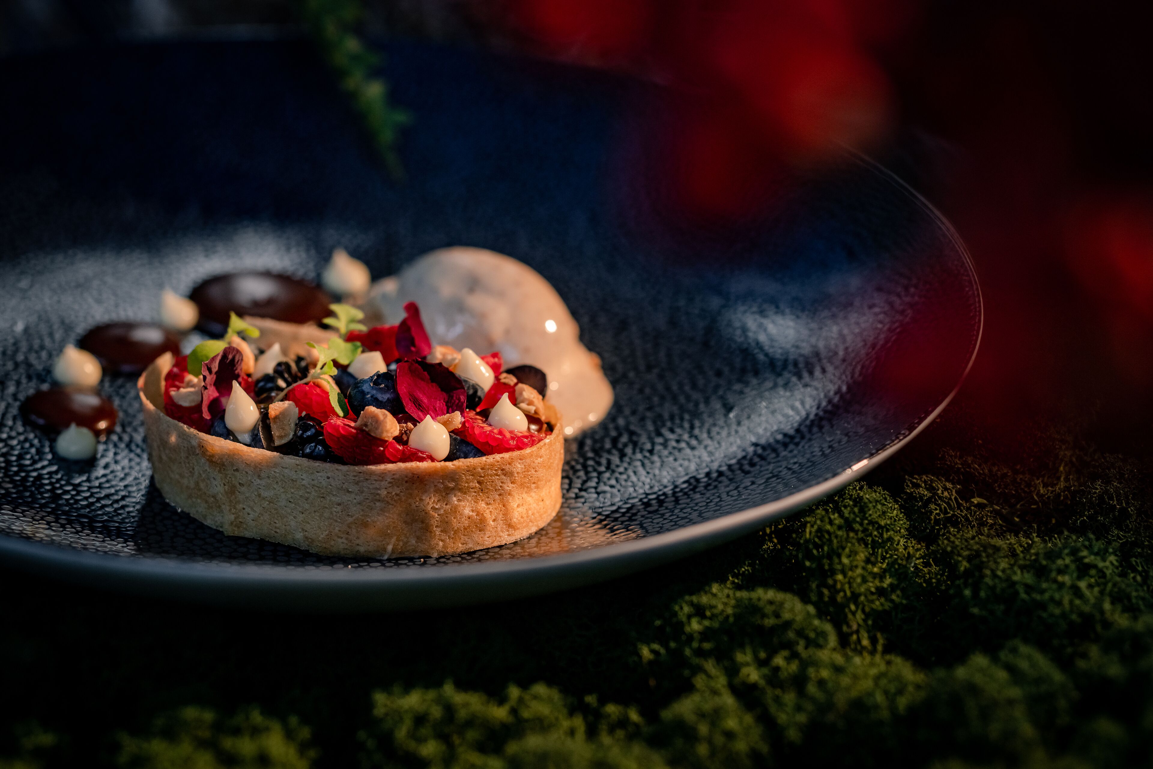 Ein Dessert auf einer tellerartigen Platte vor dunklem Hintergrund.