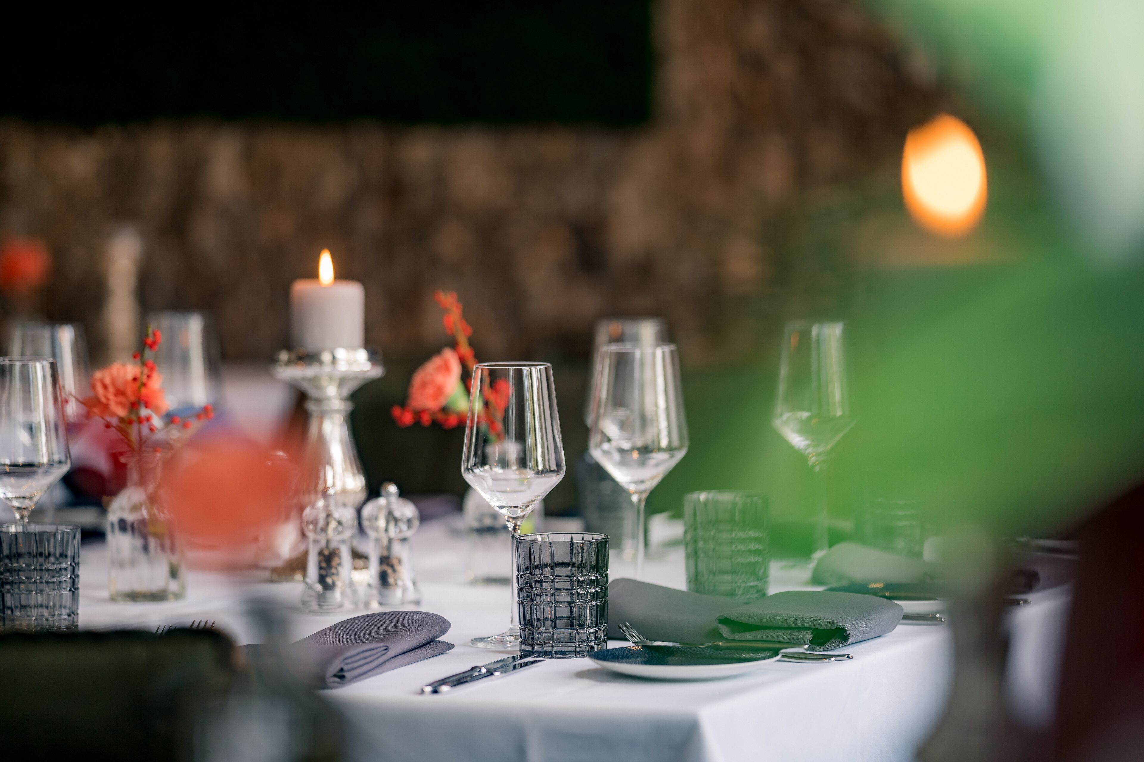 Une table mise pour un repas, avec de la belle verrerie, une bougie et un vase rempli de fleurs.