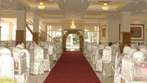 Un hall de hotel con una alfombra roja que conduce a una zona de recepción, sillas blancas, candelabros y una escalera.