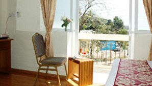 Una habitación con cama, una silla, una mesita y una ventana con cortinas.