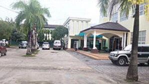 Vista de la calle con un edificio que tiene un acceso cubierto, palmeras y coches aparcados.