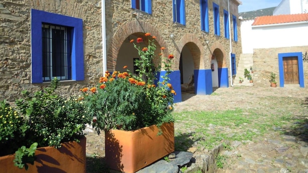 Un edificio de piedra con marcos y arcos azules, rodeado de macetas con flores naranjas.