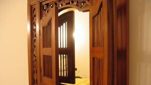 Espejo de madera con elaborados grabados que refleja una habitación con una cama y una ventana.