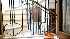 Vista a través de una ventana con barandilla de metal, una escalera y una puerta al fondo.