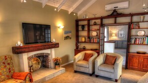 A cozy living room with a fireplace, comfortable seating, a bookshelf, and a television. - Gardenview Guest House (Gqeberha (Port Elizabeth))