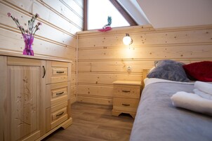 Un dormitorio con paneles de madera, una cama, mesita de noche, cómoda y un ventanal con vistas.