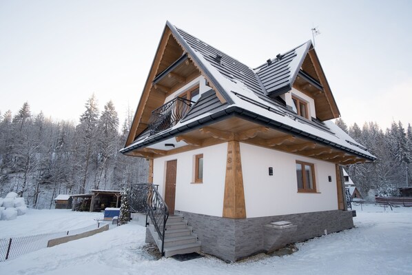 A chalet-style house with a steeply pitched roof, wooden beams, and a balcony. - Domki przy Potoku (Poronin)