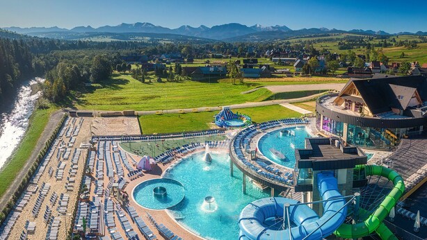 Ein Wasserpark mit großem Pool, Rutschen und einer malerischen Bergkulisse.