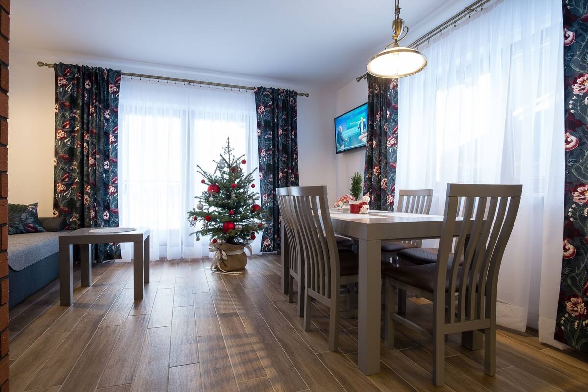 Ein Essbereich mit Holztisch und Stühlen, einem Weihnachtsbaum und einem Fernseher an der Wand.