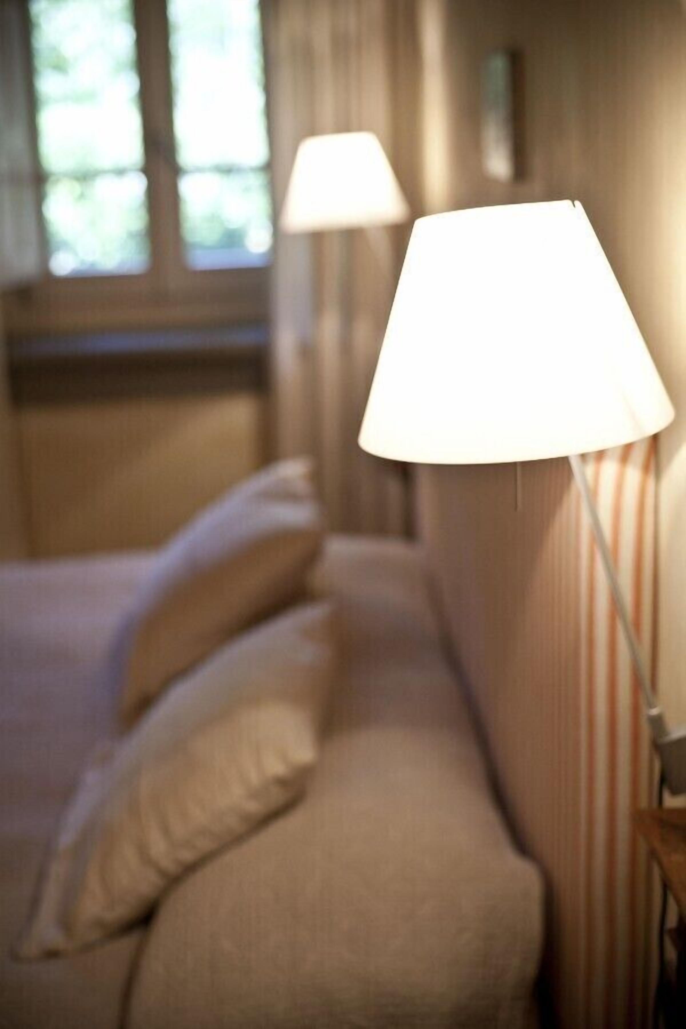 Una habitación de hotel con una cama, almohadas, una mesita de noche y una lámpara.