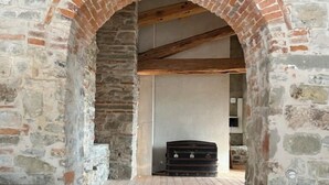 Une pièce aux murs de pierre, avec une arche en briques donnant sur un escalier en bois.