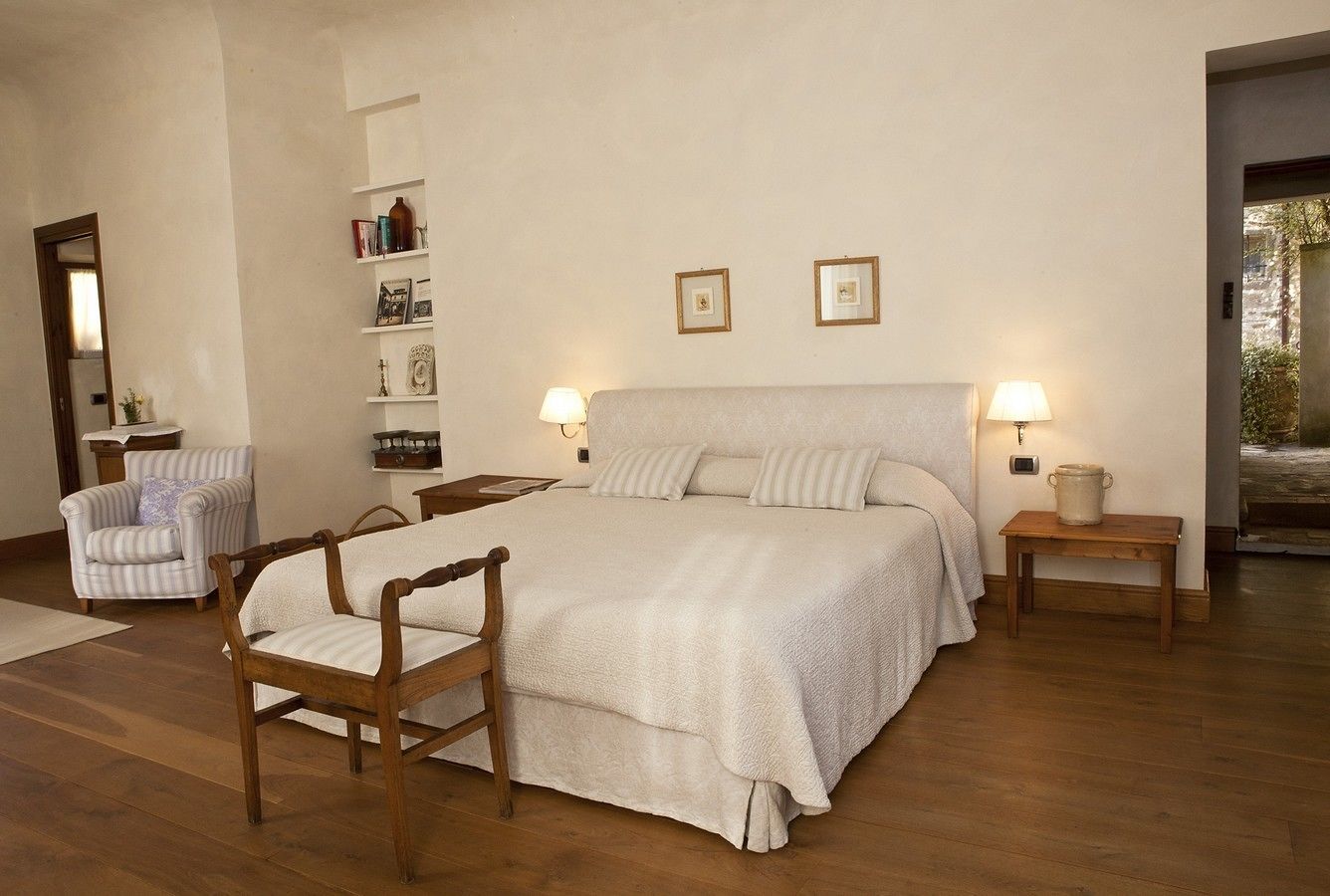 A bedroom with a large bed, two bedside tables with lamps, a wooden chair, and a bookshelf.