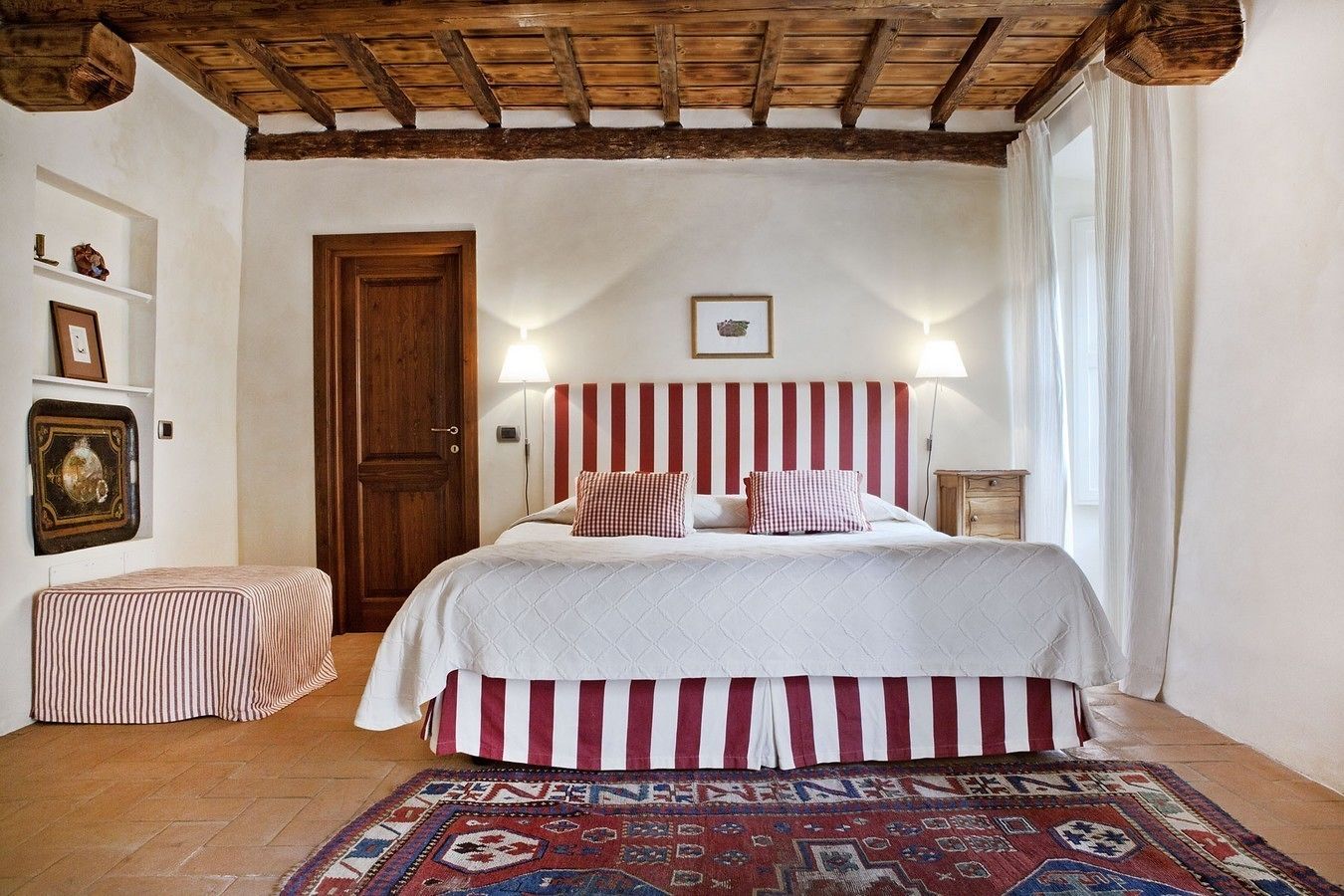 A bedroom with a wooden ceiling, a bed with striped bedding, a patterned rug, and a door.