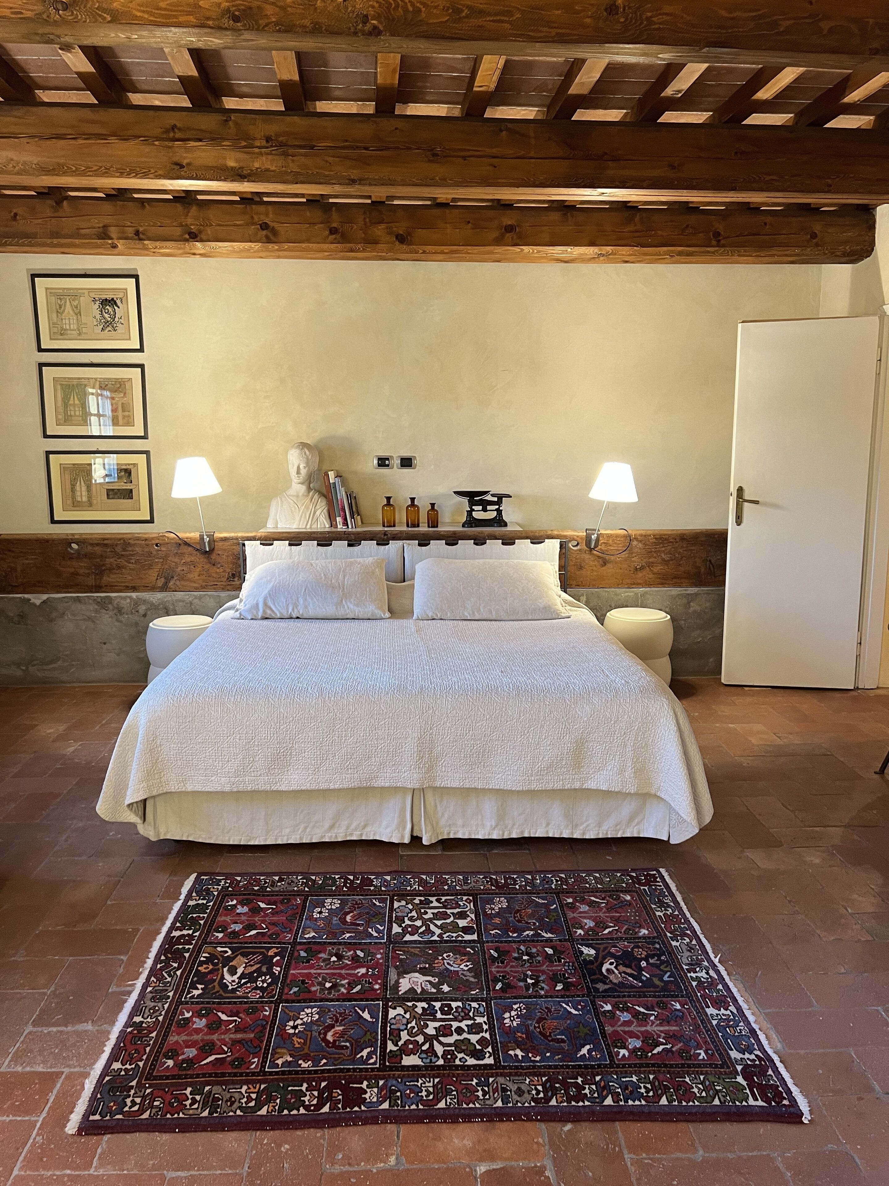 A bedroom with a large bed, two bedside lamps, a white door, and a patterned rug.